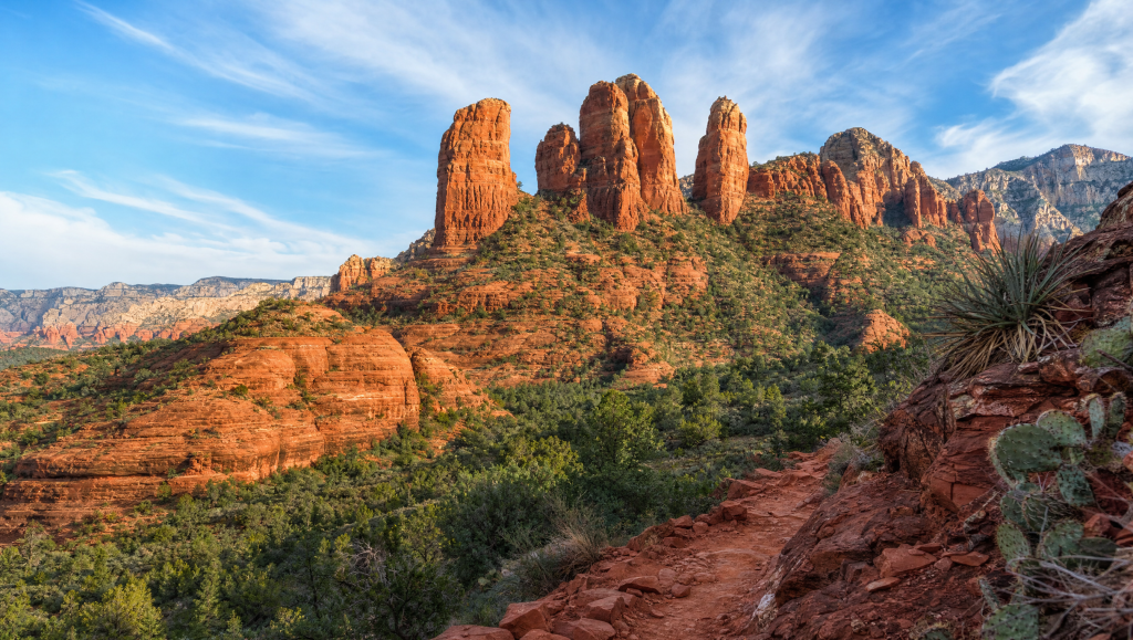 Scenic view of dramatic red rock formations and green desert vegetation under a blue sky in Sedona, Arizona.