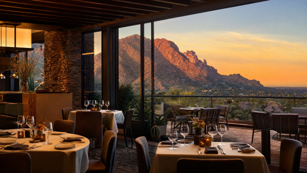 Elegant indoor-outdoor restaurant dining room with set tables overlooking a scenic sunset and Camelback Mountain in Paradise Valley.