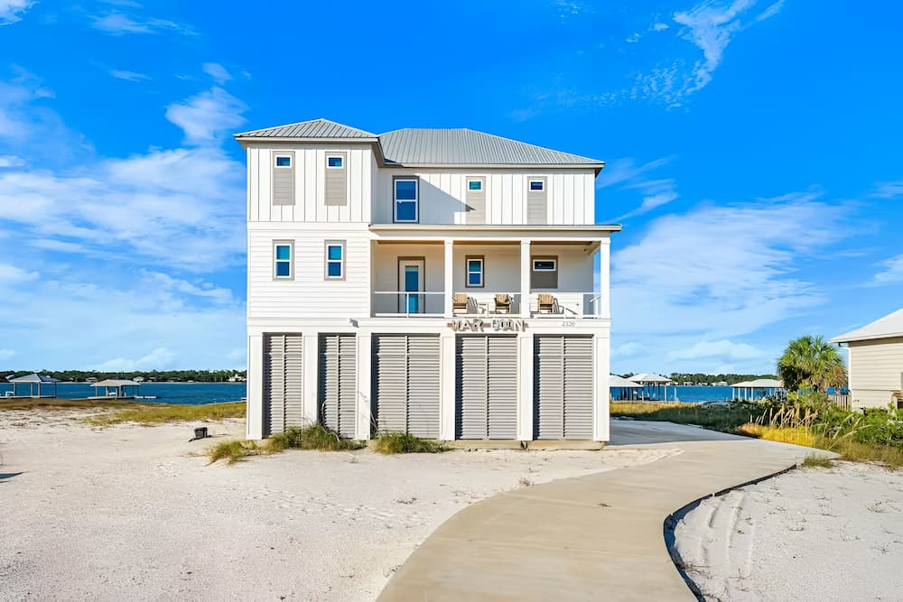 Three-story white coastal home with covered balcony beside a waterfront