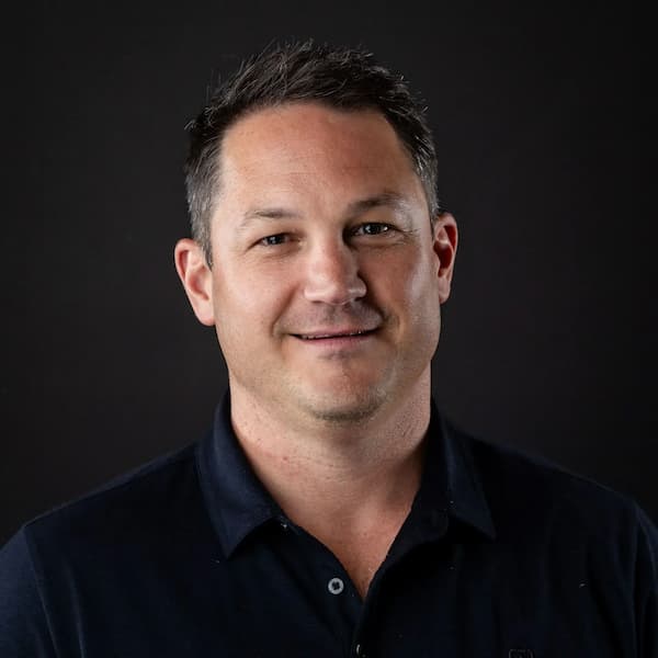 Headshot of smiling man in dark polo shirt against black background
