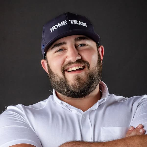 Headshot of smiling bearded man in white polo and Home Team cap